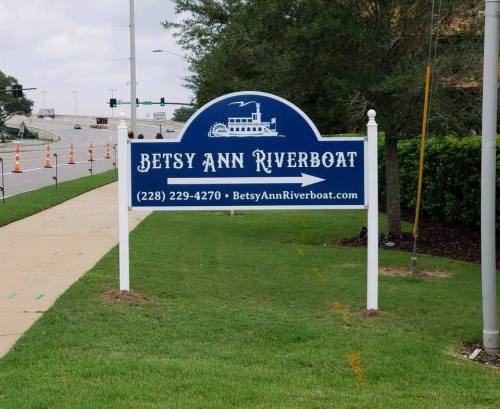 Sign for Betsy Ann Riverboat with contact information and website, set against a grassy area and cloudy sky.