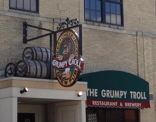 Sign for The Grumpy Troll Restaurant & Brewery, featuring a troll logo and barrels in front of a brick building.