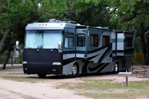 A large, modern RV parked on a gravel site surrounded by trees.