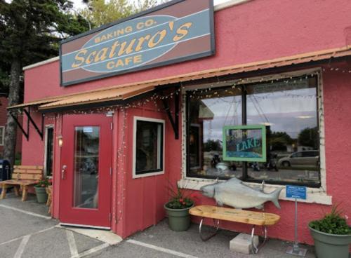 Exterior of Scaturro's Cafe, featuring a red door, sign, and decorative lights, with a fish sculpture and potted plants.