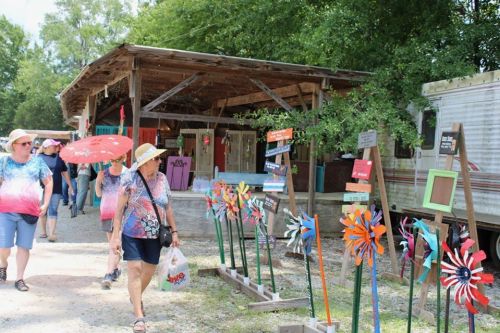 A group of people strolls past colorful windmills and a rustic market under sunny skies.