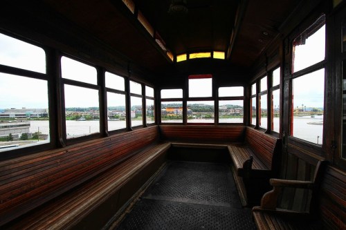Interior of a vintage train car with wooden benches and large windows, overlooking a scenic view outside.