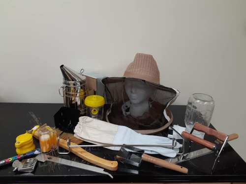 A collection of beekeeping tools, including a smoker, hive tools, and protective gear, arranged on a table.