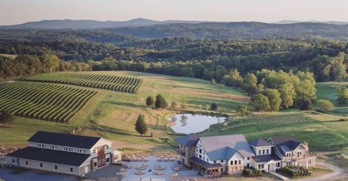 A scenic view of rolling hills, vineyards, and a pond, with a modern building in the foreground.
