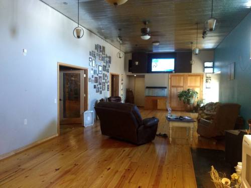 Spacious living room with wooden floors, two armchairs, a TV, and a wall of framed photos.