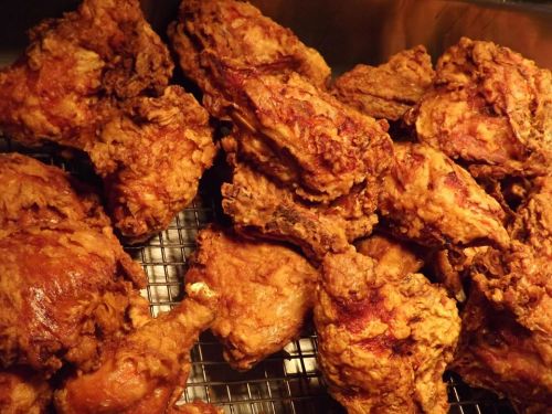 A close-up of crispy, golden-brown fried chicken pieces piled on a wire rack.