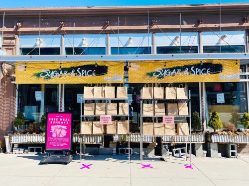 Exterior of "Sugar & Spice" restaurant with takeout bags hanging and a sign for free meal Sundays.