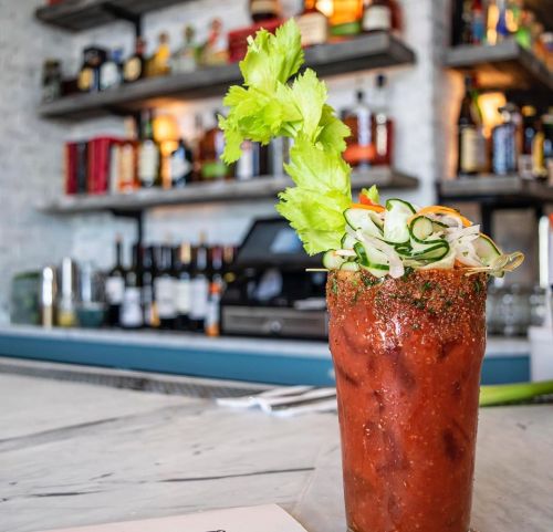 A vibrant Bloody Mary garnished with celery and cucumber, set against a backdrop of a well-stocked bar.