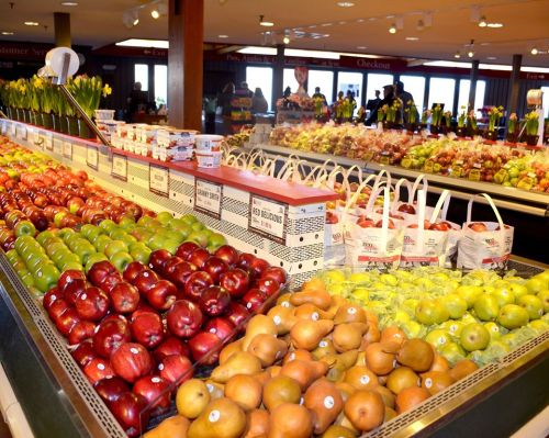 A vibrant display of various apples, pears, and other fruits in a grocery store, with shoppers in the background.