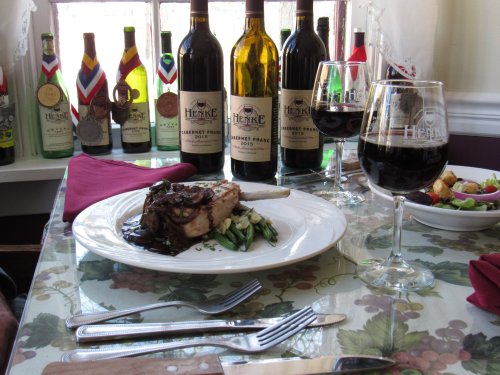 A plate of lamb chop with vegetables, surrounded by wine bottles and glasses on a decorated table.