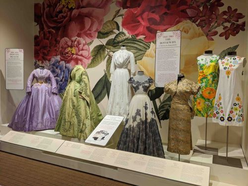 A display of various historical dresses against a floral backdrop, showcasing diverse styles and designs.
