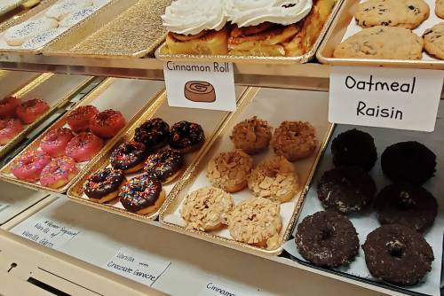 A display of assorted donuts, including cinnamon rolls, oatmeal raisin, and various frosted options with sprinkles.