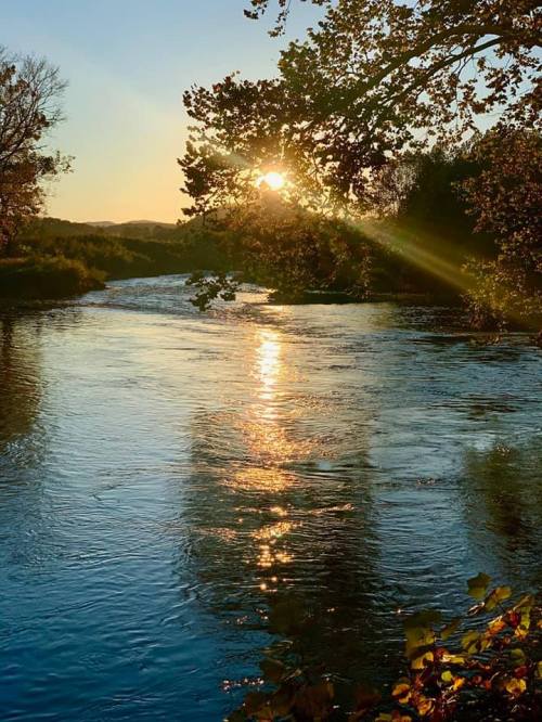 Sunset over a tranquil river, with golden light reflecting on the water and trees framing the scene.