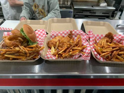 Three trays of food: a burger with lettuce, fried chicken, and fries, all served in paper-lined containers.
