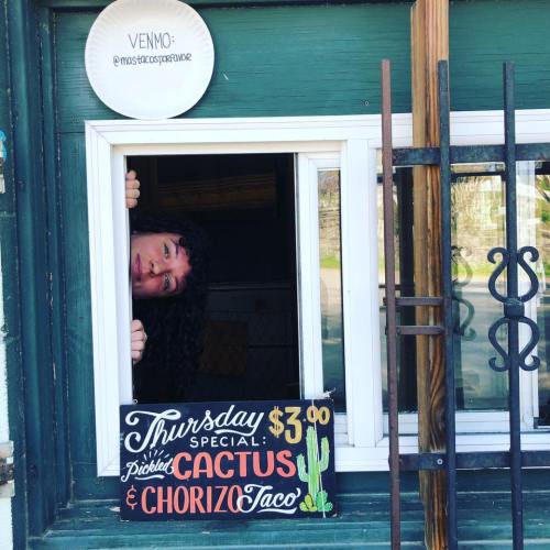 A person peeks out from a window with a sign advertising a special taco deal for Thursday.