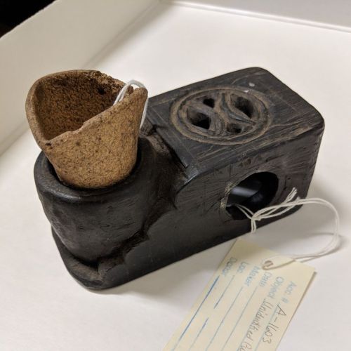 A small, dark wooden object with a cork top and a tag, resembling a vintage tool or container.