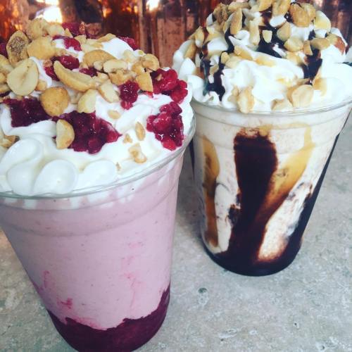 Two delicious milkshakes topped with whipped cream, nuts, and drizzles of chocolate and raspberry sauce.