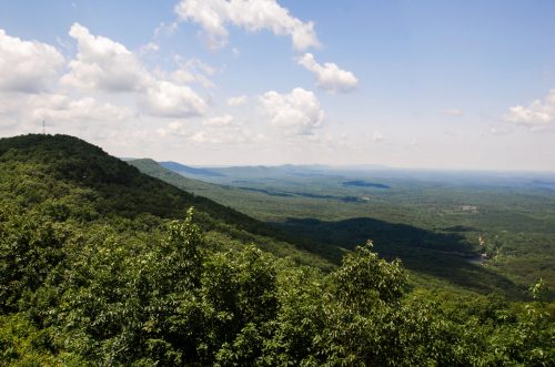 A panoramic view of lush green mountains under a partly cloudy sky, stretching into the distance.