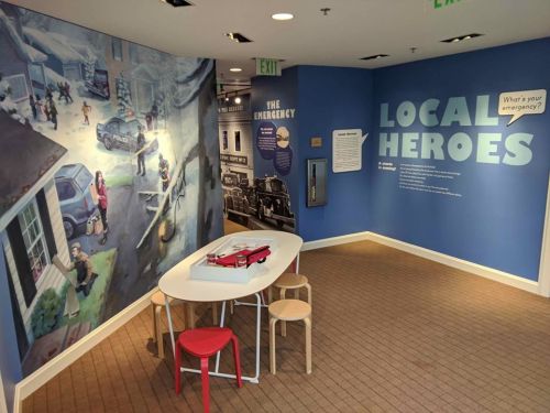 A colorful exhibit titled "Local Heroes" featuring a mural and a play area with a table and chairs.