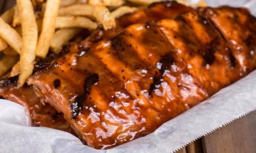 A close-up of glazed barbecue ribs served with crispy French fries on a white paper-lined tray.