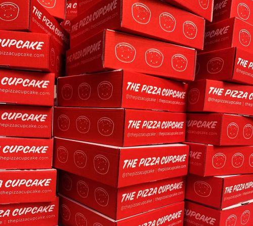 A stack of red pizza cupcake boxes featuring a smiling face design and the brand name prominently displayed.