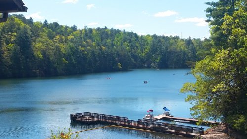 A serene lake surrounded by lush trees, with a dock and small boats on the water under a clear blue sky.