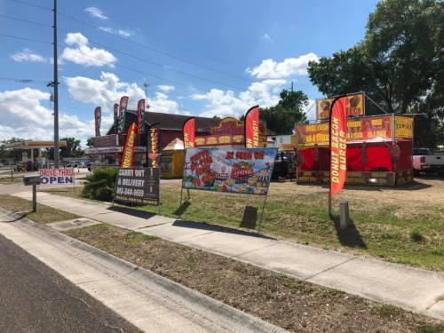 Colorful banners and signs outside a food establishment, with a clear blue sky and a few clouds in the background.