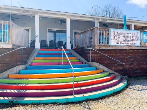 Colorful steps lead up to an ice cream shop with a sign, surrounded by outdoor seating and string lights.