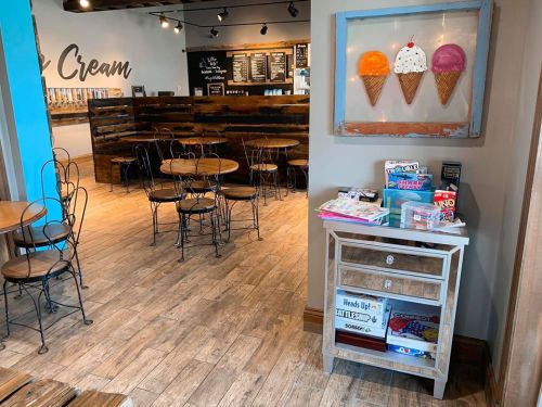 A cozy ice cream shop interior with wooden tables, a colorful ice cream art piece, and a game station in the corner.