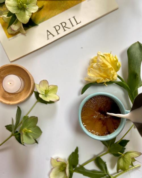 A cup of coffee with milk, surrounded by flowers and a candle, with an "April" calendar in the background.