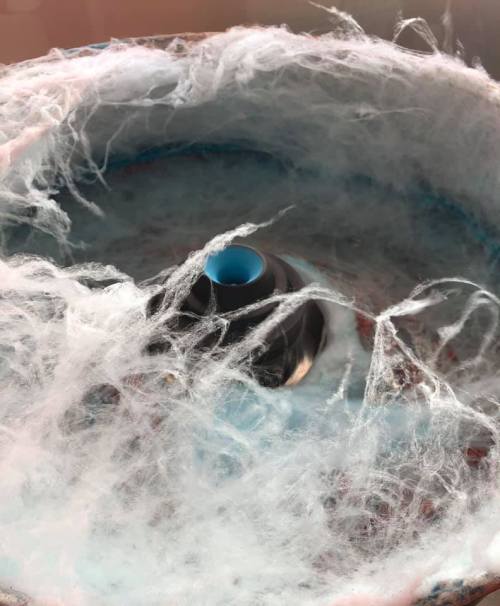 Close-up of a cotton candy machine with fluffy, spun sugar around the central spindle.