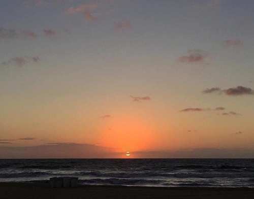 A serene sunset over the ocean, with vibrant orange and pink hues in the sky and gentle waves in the foreground.