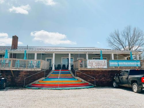 A colorful staircase leads to a charming ice cream shop with outdoor seating and a bright blue sky above.