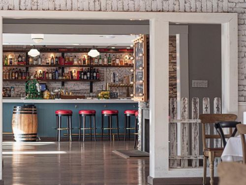 A view of a restaurant bar with red stools, shelves of liquor, and a rustic interior design.