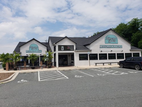 Exterior of Naughty Dogs Restaurant Pub & Grill, featuring a light-colored building and outdoor seating area.