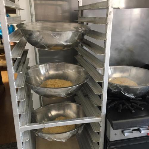 Four large metal bowls with dough resting on a rack in a kitchen, next to a stove.