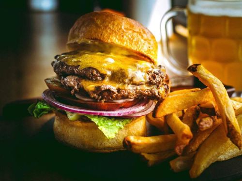 A juicy cheeseburger with lettuce, tomato, and onion, served with crispy fries and a glass of beer.