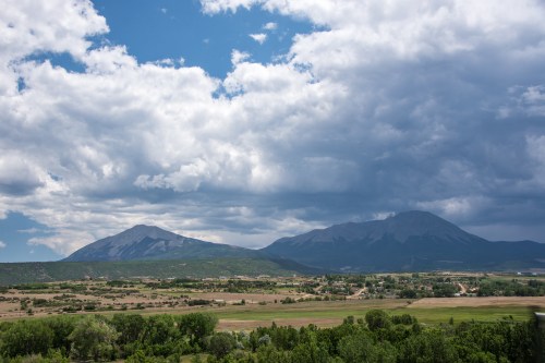 A scenic view of mountains under a partly cloudy sky, with green fields and a small town in the foreground.
