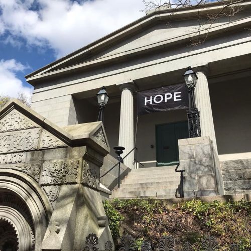 A stone building with columns and a banner reading "HOPE" hanging above the entrance, surrounded by greenery.