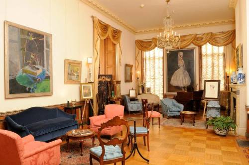 A stylish room with elegant furniture, artwork on the walls, and large windows draped with golden curtains.