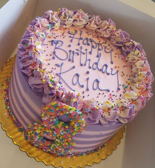 A purple birthday cake with frosting, sprinkles, and "Happy Birthday Kaia" written on top.