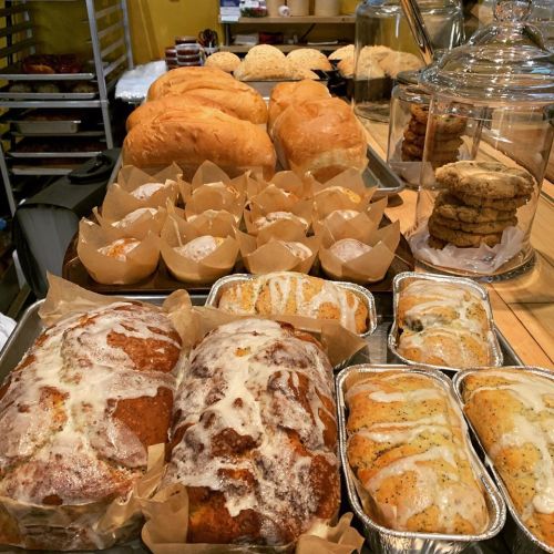 A variety of baked goods including loaves of bread, muffins, and cookies displayed on a wooden table.