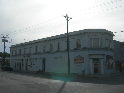A blue, two-story building with large windows, located on a street with power lines and parked vehicles nearby.