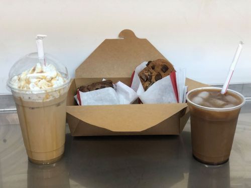 A creamy iced coffee and a frothy drink sit beside a box of three assorted chocolate cookies.