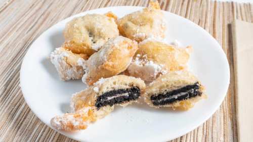 A plate of deep-fried Oreos dusted with powdered sugar, some cut in half to reveal the creamy filling.