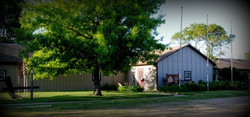 A quaint building with a gray exterior, surrounded by greenery and a large tree, set in a peaceful outdoor environment.