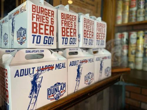 Takeout boxes labeled "Burger, Fries & Beer To Go!" stacked on a counter at Dunlap Cafe.