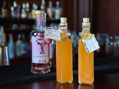 Two bottles of orange cocktails with tags, in front of a bottle of Glendalough Rose Gin on a bar.