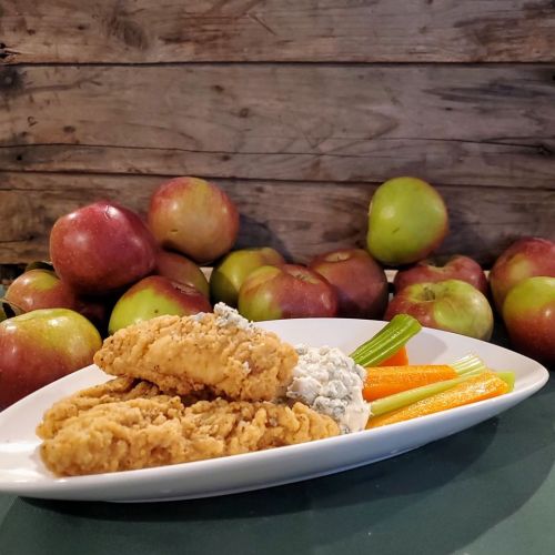 Plate of crispy chicken tenders with celery, carrots, and blue cheese dip, surrounded by fresh apples.