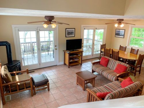 Cozy living area with striped sofas, wooden furniture, a TV, and large windows overlooking a deck.